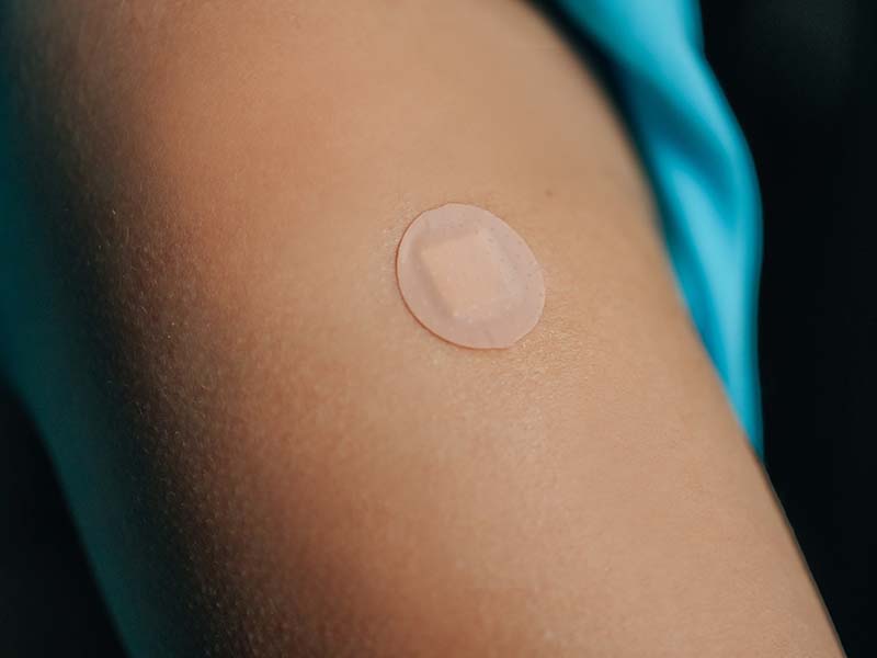 Photo of an upper arm with a small round bandage after having a medical shot.